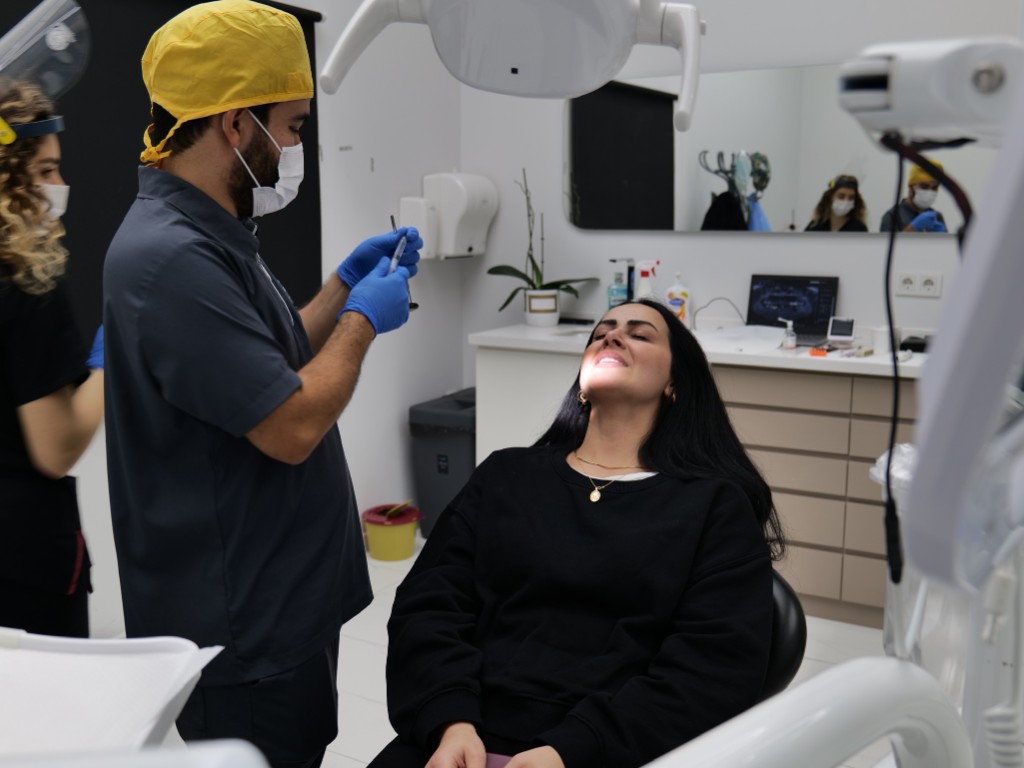 Patient relaxed in the dental chair while the dentist works under bright clinical lighting.